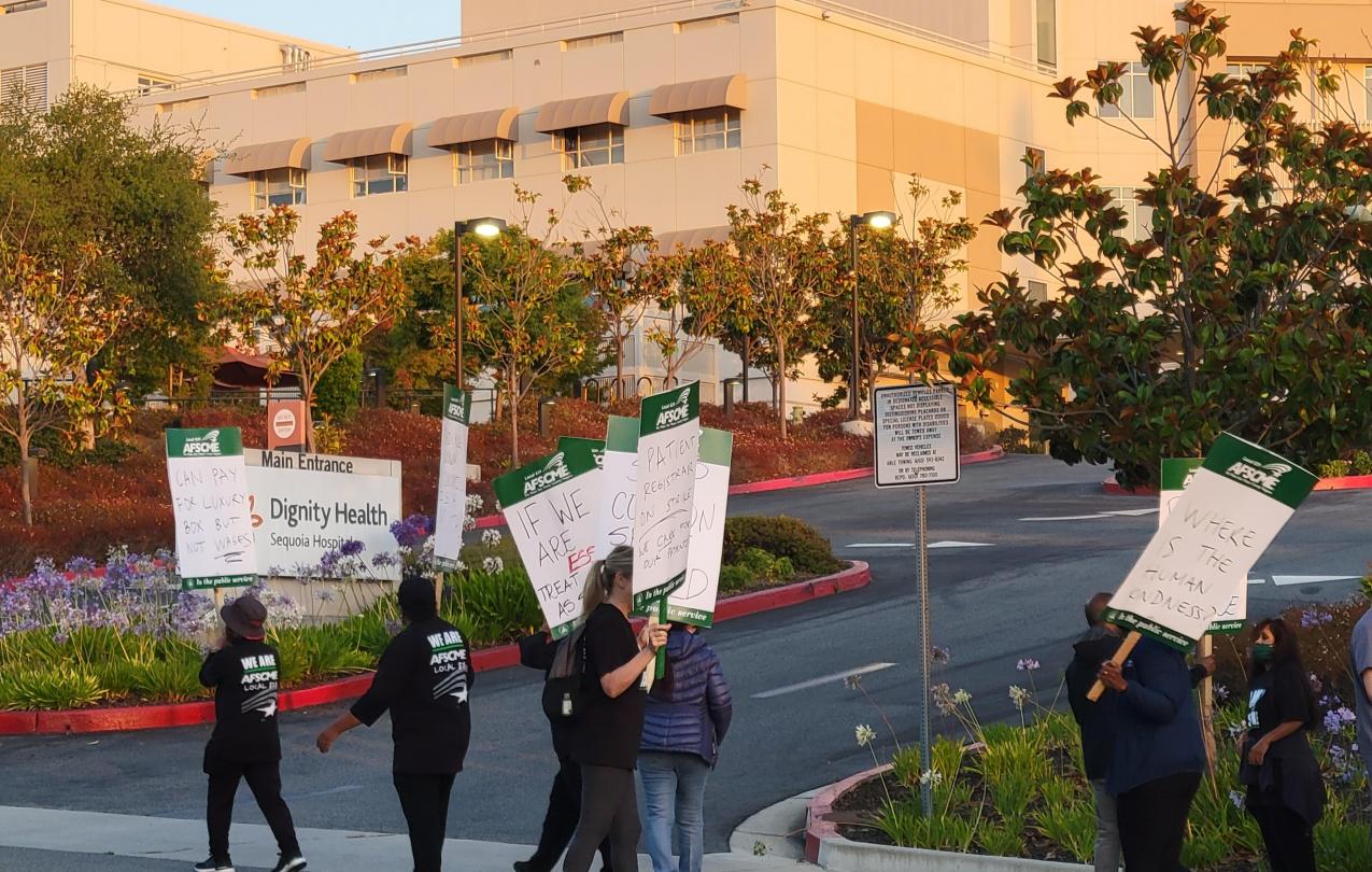 Image of workers holding picket signs and walking past a hospital